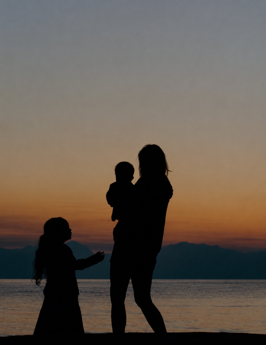 Family silhouetted against a peaceful sunset over the ocean
